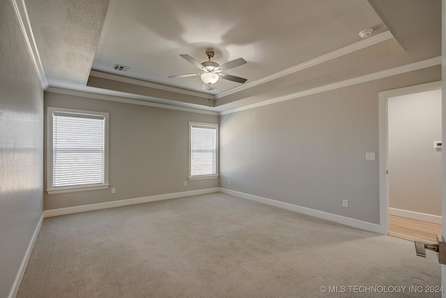 empty room featuring a raised ceiling, crown molding, light carpet, and ceiling fan