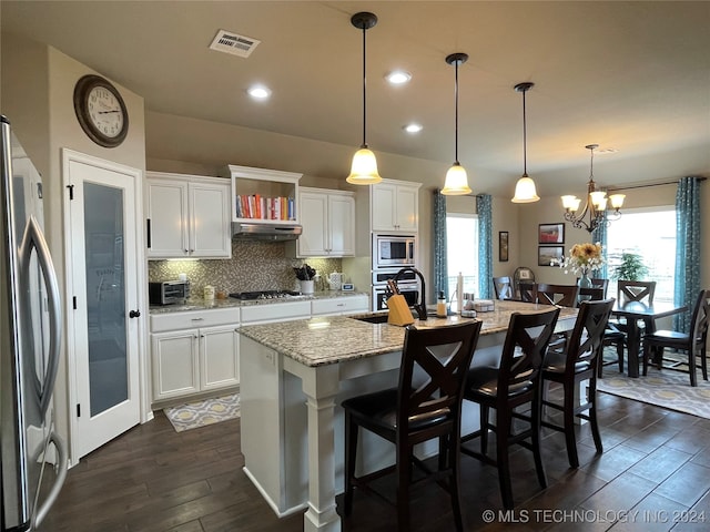 kitchen featuring hanging light fixtures, white cabinetry, an island with sink, stainless steel appliances, and an inviting chandelier