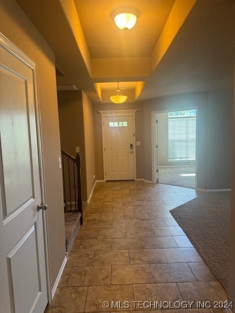 entryway with a raised ceiling and light carpet