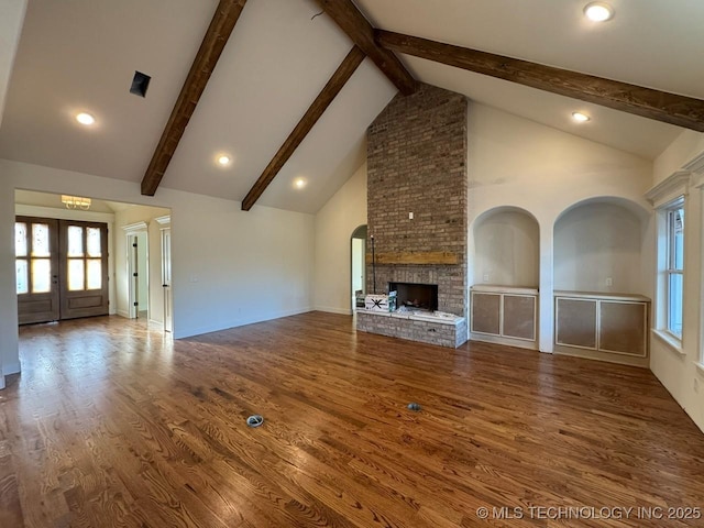 unfurnished living room with beam ceiling, french doors, a brick fireplace, wood finished floors, and high vaulted ceiling