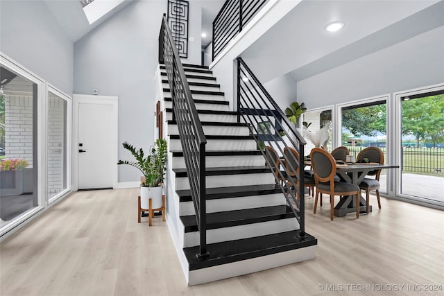 stairs featuring hardwood / wood-style floors, a skylight, and high vaulted ceiling