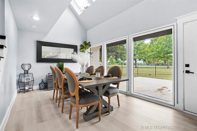 dining area with light hardwood / wood-style flooring, a skylight, and high vaulted ceiling