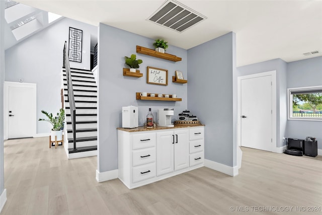 bar with light hardwood / wood-style flooring and white cabinets