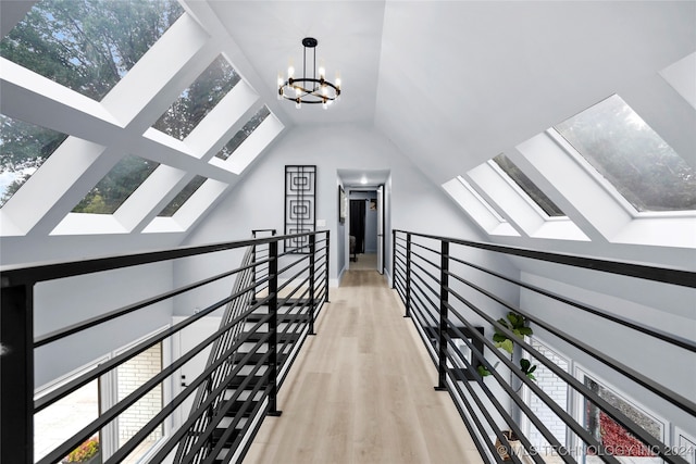 corridor featuring vaulted ceiling with skylight, a chandelier, and light hardwood / wood-style flooring