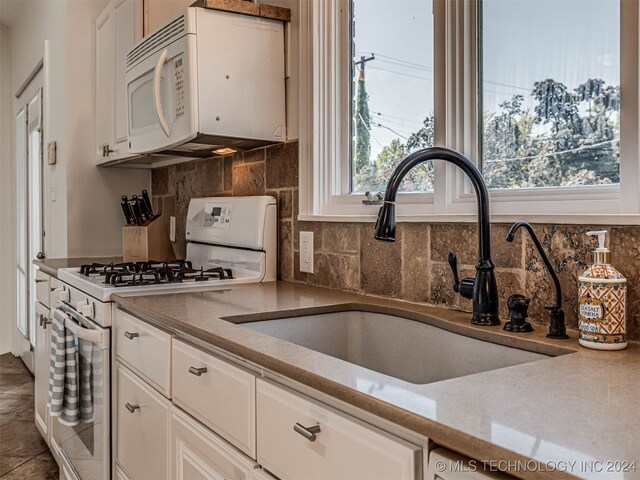 kitchen with white appliances, backsplash, sink, and white cabinetry