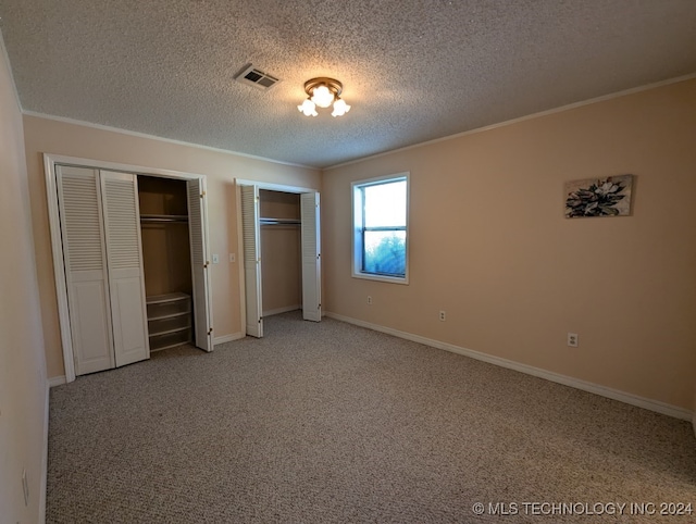 unfurnished bedroom with carpet floors, crown molding, a textured ceiling, and multiple closets