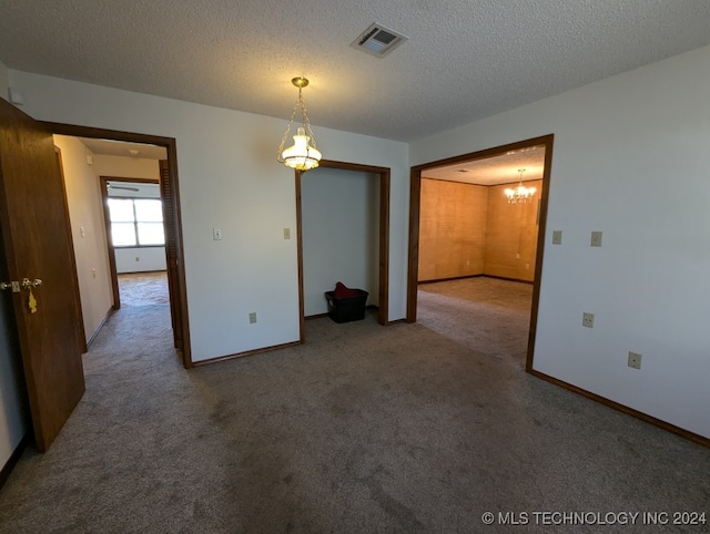 carpeted empty room with a notable chandelier and a textured ceiling