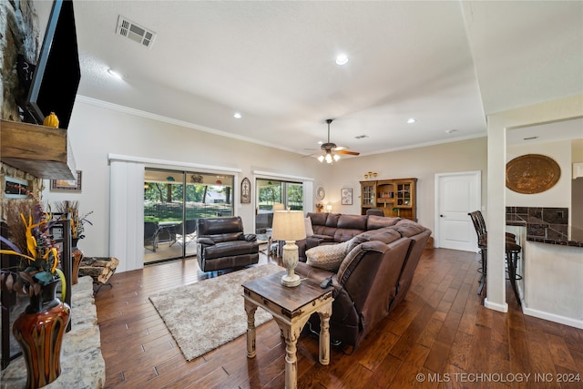 living room featuring ceiling fan, a stone fireplace, crown molding, and dark hardwood / wood-style flooring