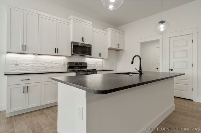 kitchen with a kitchen island with sink, black gas range oven, sink, and decorative light fixtures