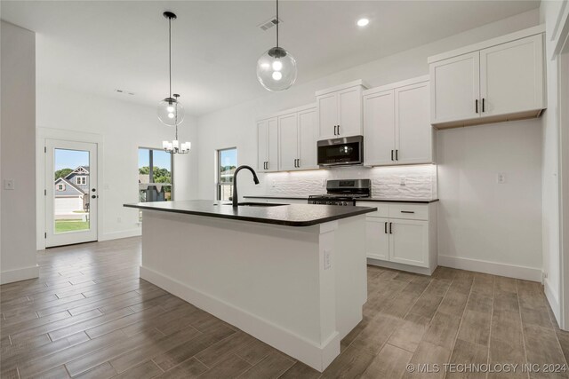 kitchen with white cabinetry, stainless steel appliances, decorative light fixtures, a center island with sink, and sink