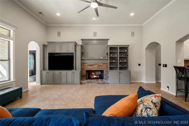 tiled living room featuring ceiling fan, crown molding, a wealth of natural light, and a stone fireplace