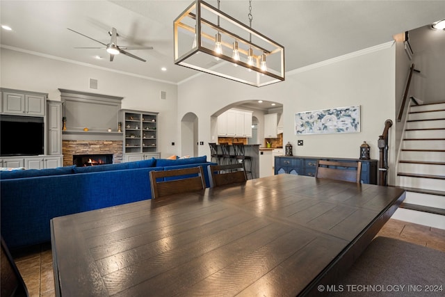 dining area with a stone fireplace, ornamental molding, built in shelves, dark tile patterned flooring, and ceiling fan with notable chandelier