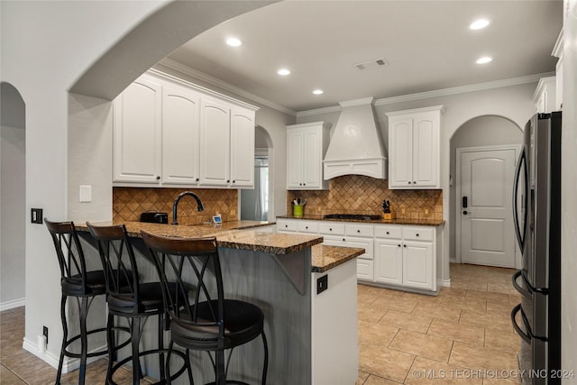 kitchen featuring fridge, white cabinetry, kitchen peninsula, a breakfast bar area, and wall chimney range hood