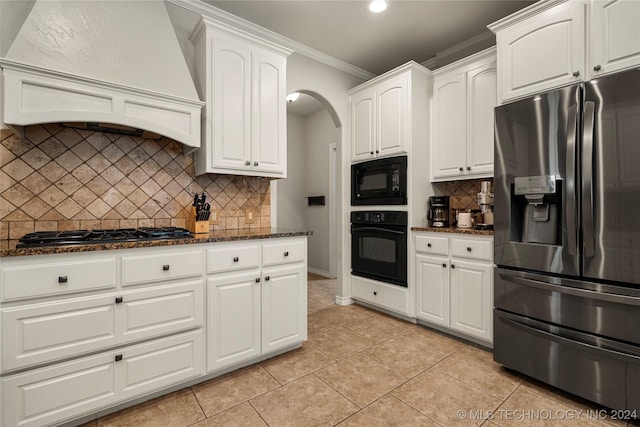 kitchen featuring white cabinets, dark stone counters, range hood, black appliances, and crown molding