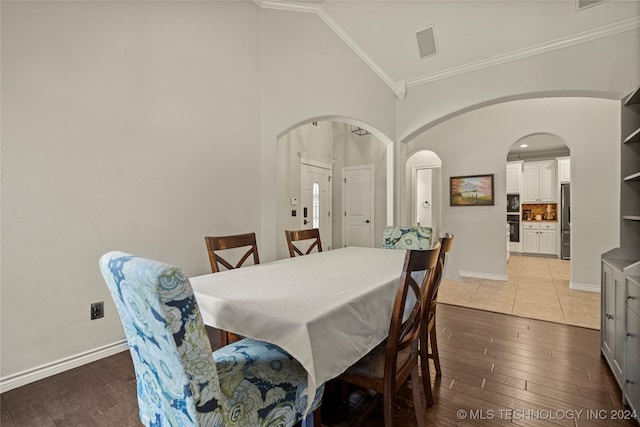 dining room featuring light wood-style floors, baseboards, arched walkways, and crown molding