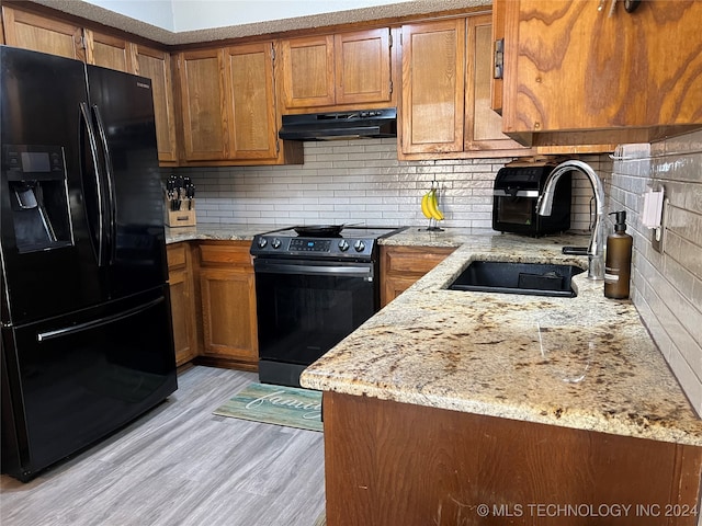 kitchen featuring light stone countertops, black appliances, light hardwood / wood-style floors, and sink