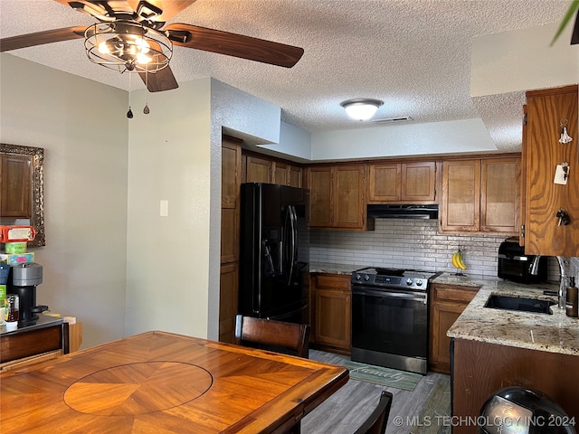 kitchen featuring decorative backsplash, stainless steel electric range, light stone countertops, sink, and black fridge