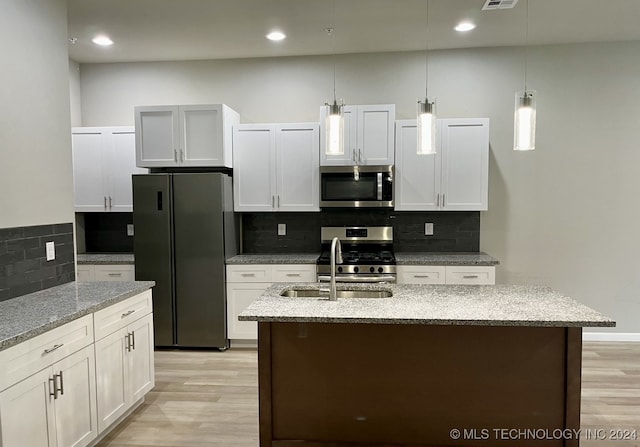 kitchen with pendant lighting, white cabinets, stainless steel appliances, a center island with sink, and light stone countertops