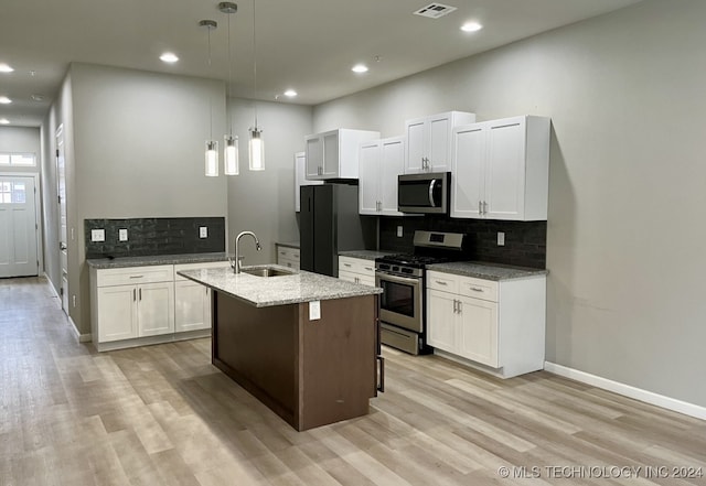 kitchen with light wood-type flooring, an island with sink, hanging light fixtures, stainless steel appliances, and light stone countertops