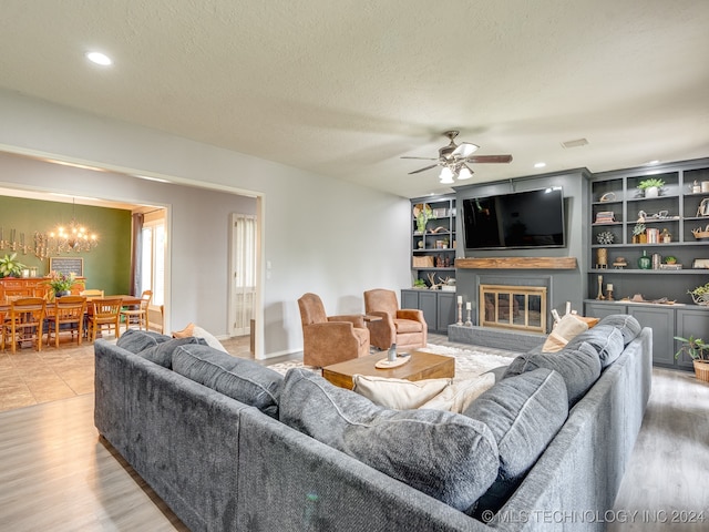 living room featuring ceiling fan with notable chandelier, light wood-type flooring, and a textured ceiling