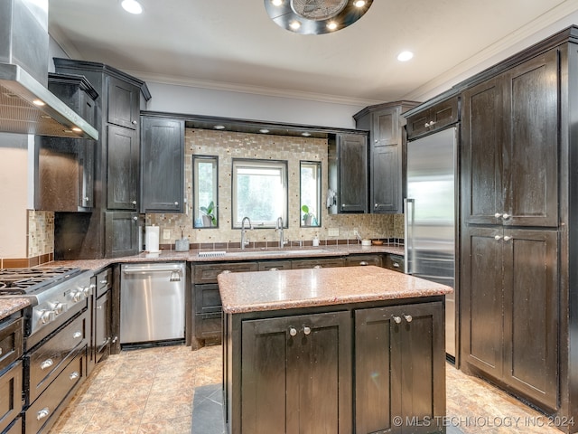 kitchen with light stone counters, a center island, tasteful backsplash, wall chimney exhaust hood, and appliances with stainless steel finishes