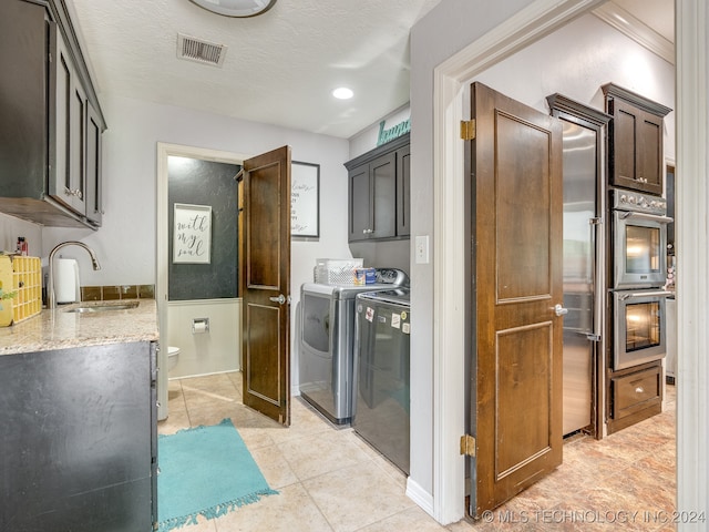 kitchen featuring light stone counters, a textured ceiling, light tile patterned flooring, sink, and separate washer and dryer