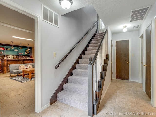 stairway with tile patterned flooring and a textured ceiling