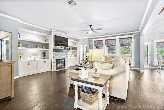 living room featuring ceiling fan, dark wood-type flooring, a stone fireplace, built in features, and crown molding