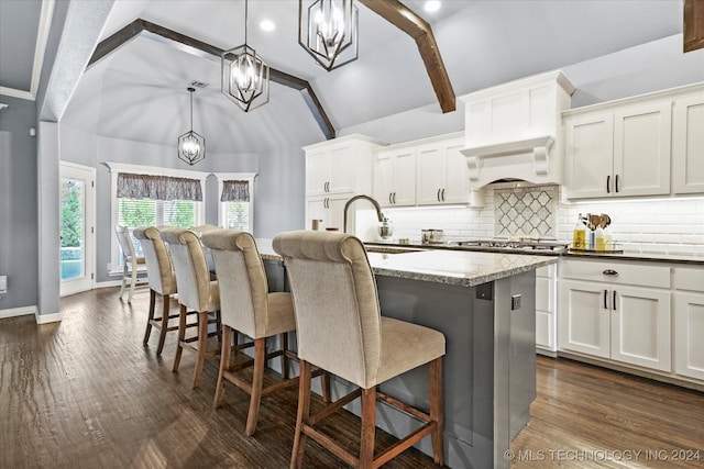 kitchen featuring white cabinetry, vaulted ceiling with beams, decorative light fixtures, a kitchen island with sink, and custom exhaust hood