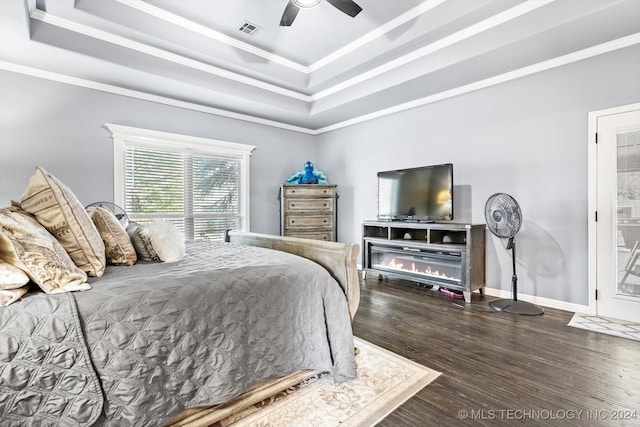 bedroom with a raised ceiling, ceiling fan, dark wood-type flooring, and ornamental molding