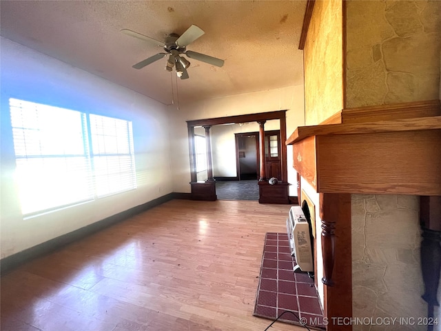 unfurnished living room with a textured ceiling, ceiling fan, a wall unit AC, and hardwood / wood-style flooring