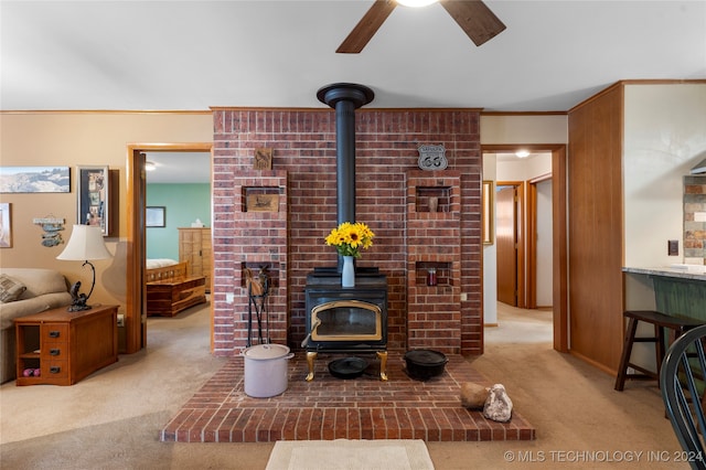 living room featuring light colored carpet, crown molding, ceiling fan, and a wood stove