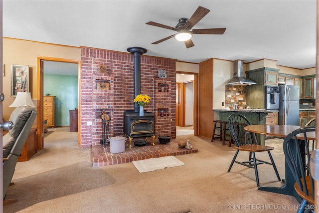 carpeted living room featuring a wood stove, ceiling fan, indoor bar, and crown molding