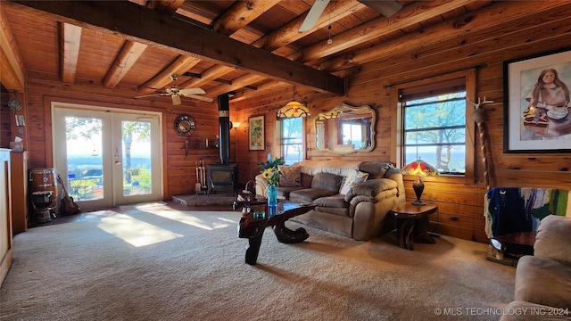 carpeted living room featuring a wood stove, beam ceiling, ceiling fan, and a wealth of natural light