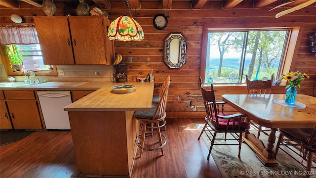 kitchen with dark hardwood / wood-style floors, sink, wooden walls, backsplash, and white dishwasher