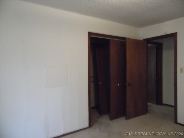 unfurnished bedroom featuring light carpet, a textured ceiling, and a closet