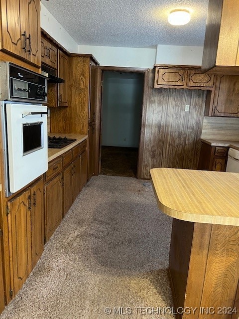 kitchen with carpet flooring, a textured ceiling, wooden walls, oven, and black gas stovetop