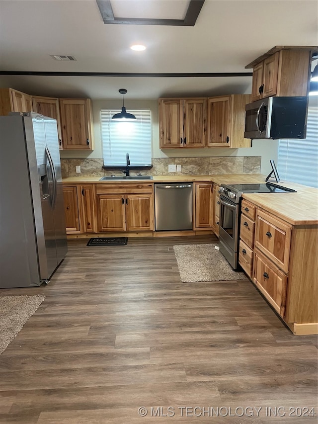 kitchen featuring stainless steel appliances, sink, hardwood / wood-style floors, pendant lighting, and decorative backsplash