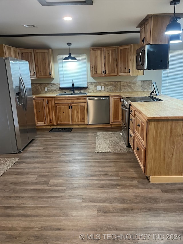 kitchen with dark wood-type flooring, sink, backsplash, pendant lighting, and appliances with stainless steel finishes