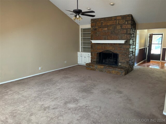 unfurnished living room featuring vaulted ceiling, a stone fireplace, a textured ceiling, ceiling fan, and built in shelves