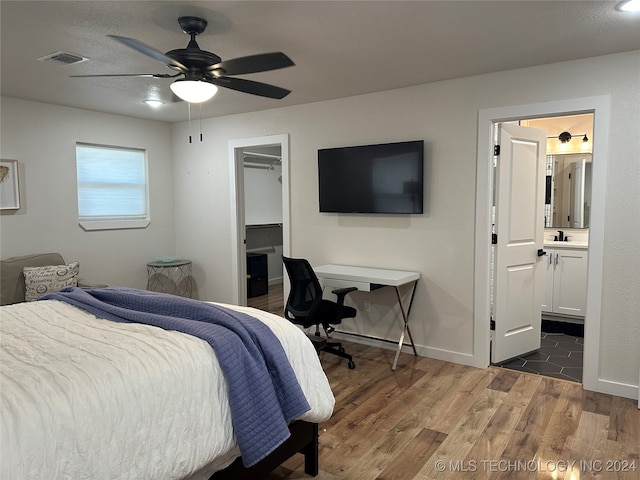 bedroom featuring ceiling fan, dark hardwood / wood-style flooring, a spacious closet, sink, and connected bathroom