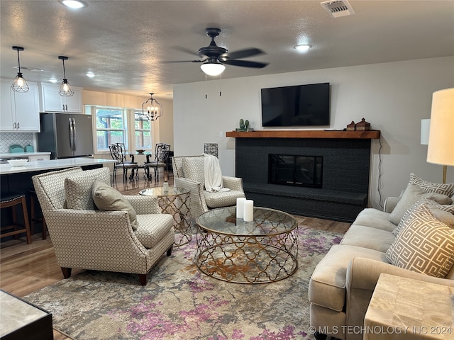 living room with hardwood / wood-style flooring, ceiling fan with notable chandelier, and a textured ceiling