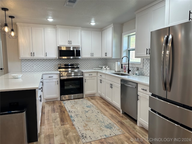 kitchen featuring sink, light hardwood / wood-style flooring, decorative light fixtures, white cabinetry, and stainless steel appliances