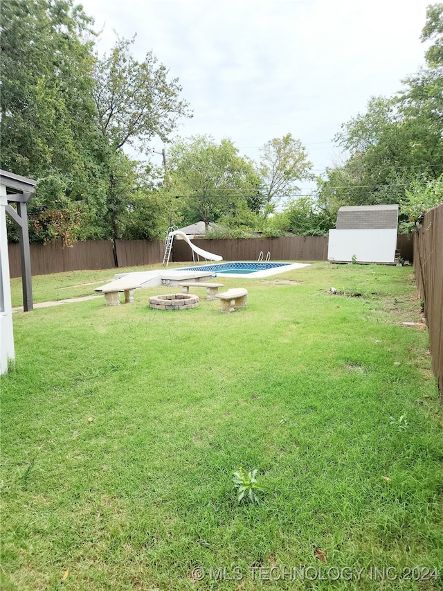 view of yard featuring a fire pit, a fenced in pool, and a storage shed