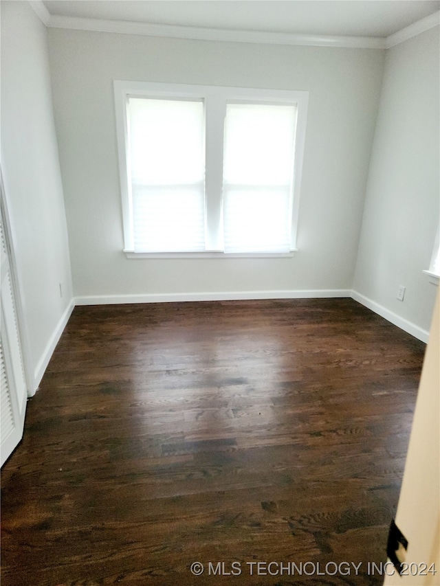 spare room featuring crown molding, dark wood-type flooring, and a wealth of natural light