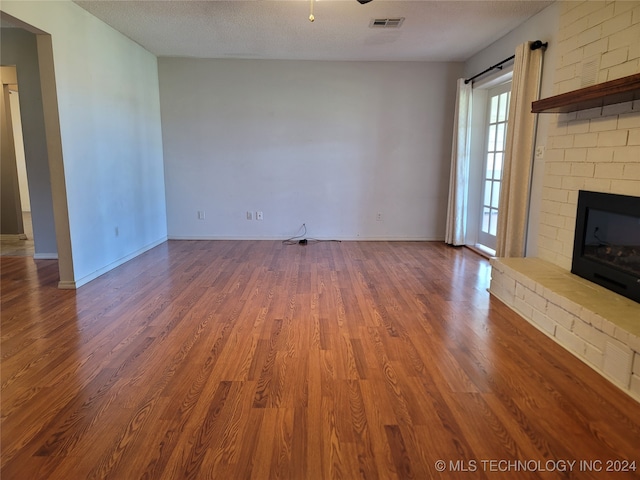 unfurnished living room with a textured ceiling, wood-type flooring, and a brick fireplace