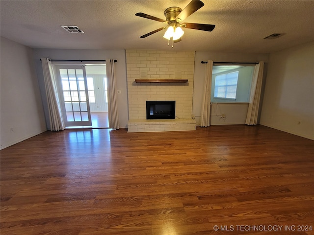 unfurnished living room with ceiling fan, a brick fireplace, a textured ceiling, and dark hardwood / wood-style floors