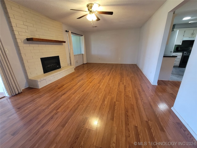 unfurnished living room with a textured ceiling, ceiling fan, a brick fireplace, and hardwood / wood-style flooring