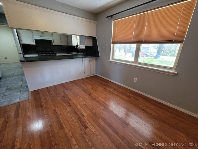 kitchen with black range oven, white cabinets, hardwood / wood-style flooring, and sink