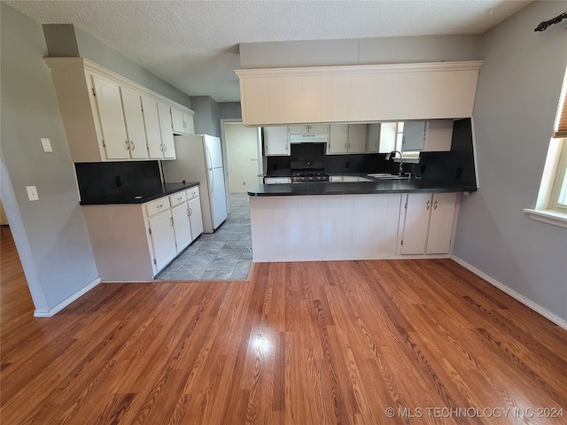 kitchen with white cabinets, kitchen peninsula, stove, white fridge, and light hardwood / wood-style flooring